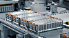 Mehrere silberne Batteriemodule liegen auf einer automatisierten Produktionslinie in einer Fabrikhalle.