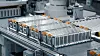Mehrere silberne Batteriemodule liegen auf einer automatisierten Produktionslinie in einer Fabrikhalle.