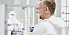 Forscher an einer Sicherheitswerkbank in einem Labor mit Person in Schutzkleidung im Hintergrund.
