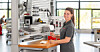 Frau arbeitet an einer industriellen Maschine in einer hellen Werkhalle.