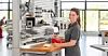 Frau arbeitet an einer industriellen Maschine in einer hellen Werkhalle.