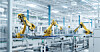 Gelbe Industrieroboter in einer modernen Fabrikhalle mit Förderbändern und weißen Metallstrukturen.