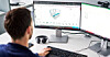 Person sitzt am Schreibtisch vor zwei Monitoren und arbeitet am Computer.